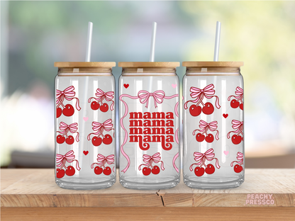 Glass cups with red cherry and bow patterns and the word 'mama' on them, each with a bamboo lid and a straw, displayed on a wooden surface with a blurred background.