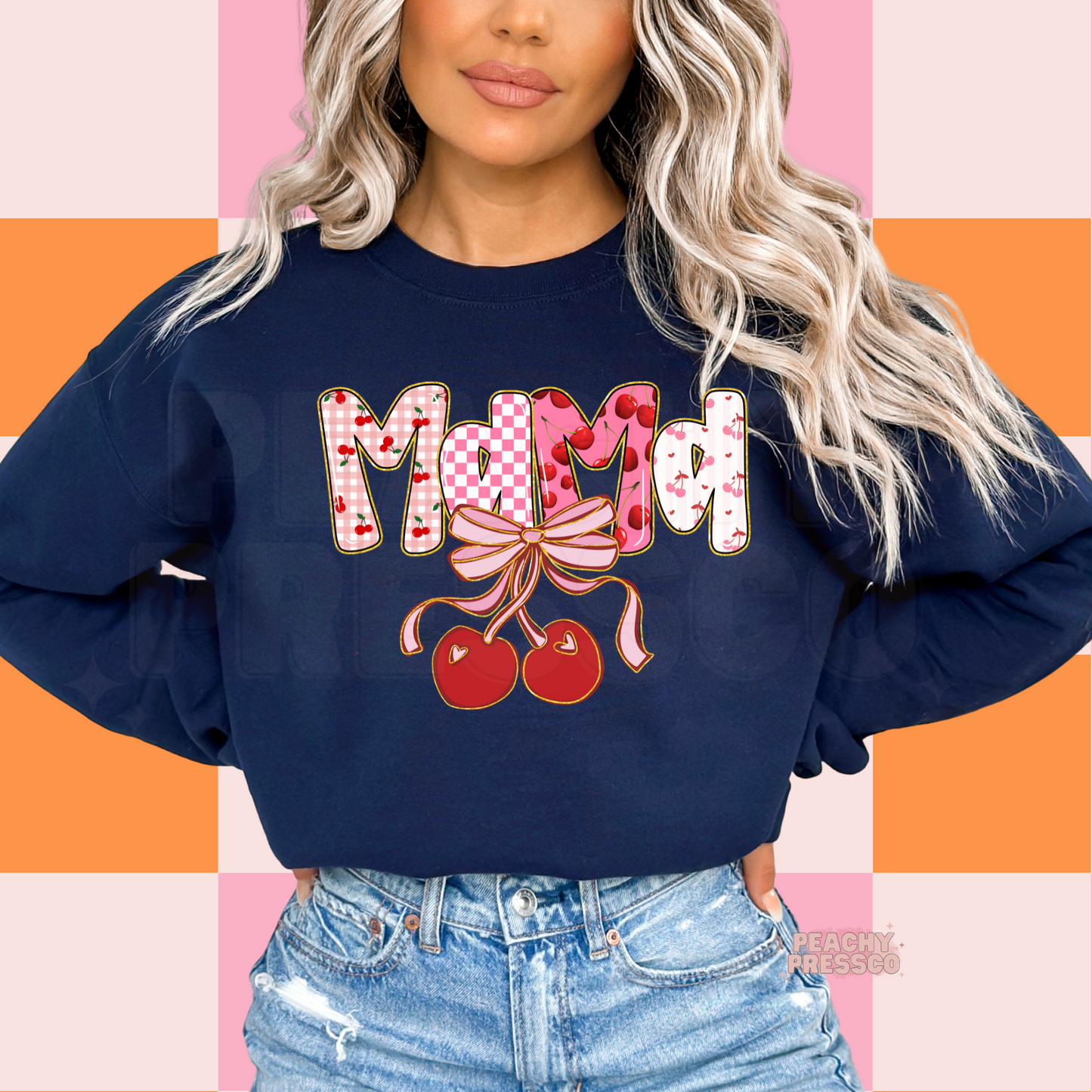 Woman wearing a navy blue sweatshirt with a colorful Mama cherry bow graphic featuring pink checkerboard, cherries, and coquette-inspired lettering.