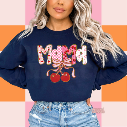 Woman wearing a navy blue sweatshirt with a colorful Mama cherry bow graphic featuring pink checkerboard, cherries, and coquette-inspired lettering.