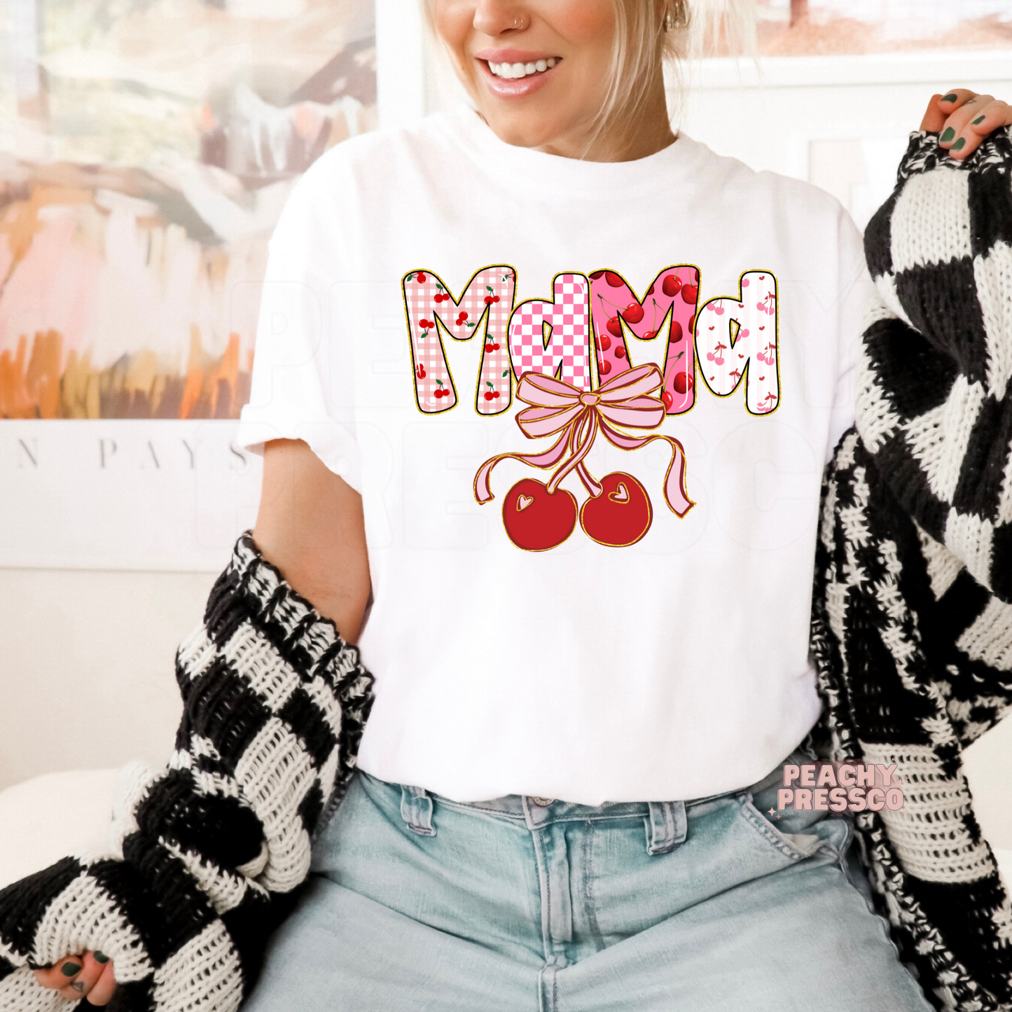 Woman wearing a white t-shirt with a Mama cherry bow graphic featuring pink bows, cherries, and playful coquette lettering.
