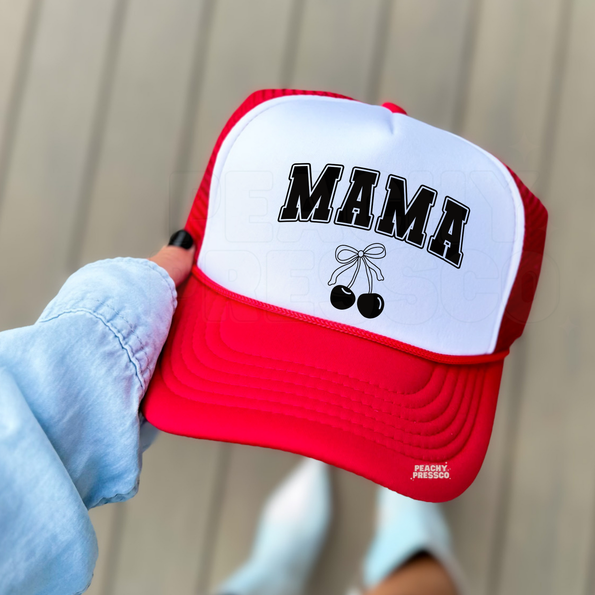 Red and white foam trucker hat featuring varsity "MAMA" lettering with a black cherry bow graphic. Stylish trucker hat for moms, Mother's Day, summer outings, lake days, vacations, and everyday wear.