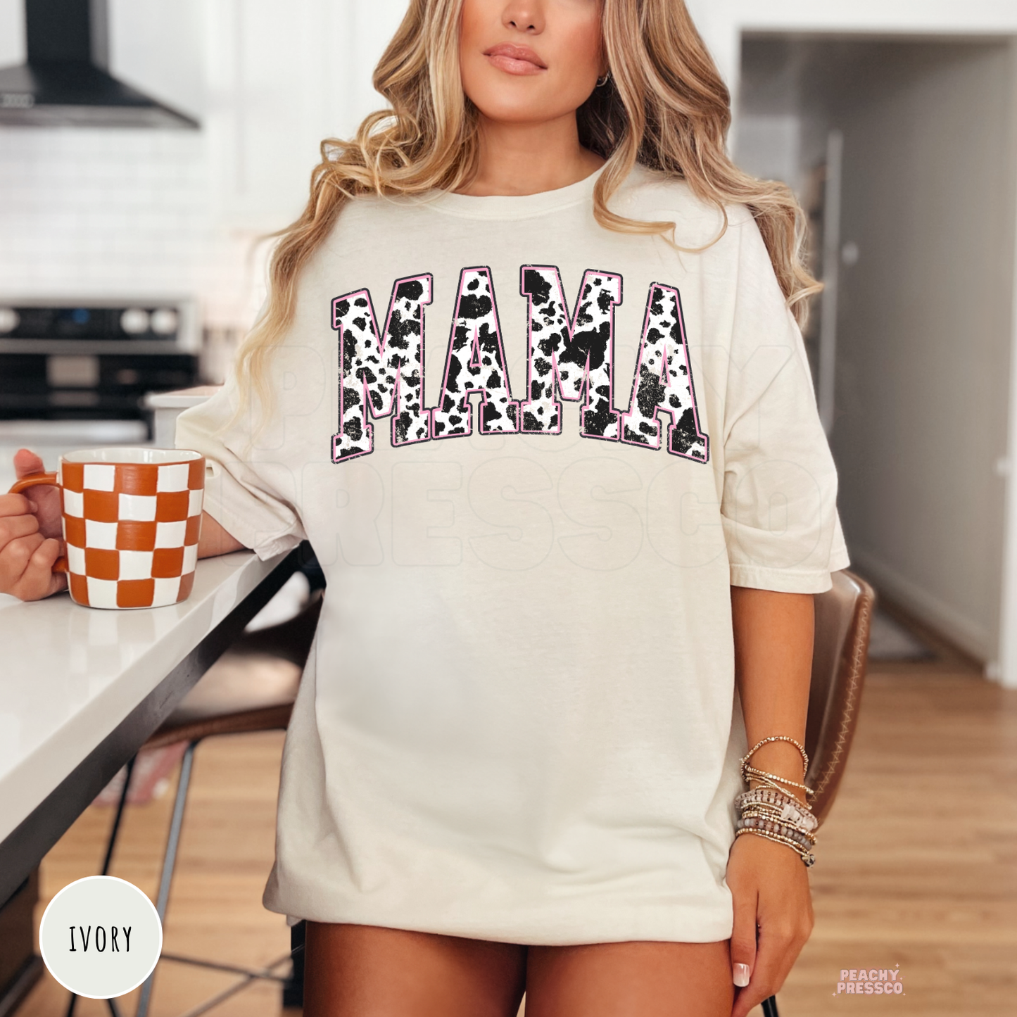 Ivory t-shirt featuring a distressed cow print "MAMA" graphic with pink detailing. Cute western mama tee for Mother's Day, birthdays, or everyday wear.