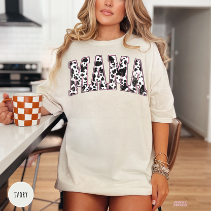 Ivory t-shirt featuring a distressed cow print "MAMA" graphic with pink detailing. Cute western mama tee for Mother's Day, birthdays, or everyday wear.