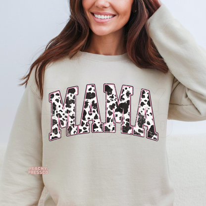 Sand crewneck sweatshirt featuring a distressed cow print "MAMA" graphic outlined in pink. A cozy western-inspired gift for moms who love farmhouse and country style.
