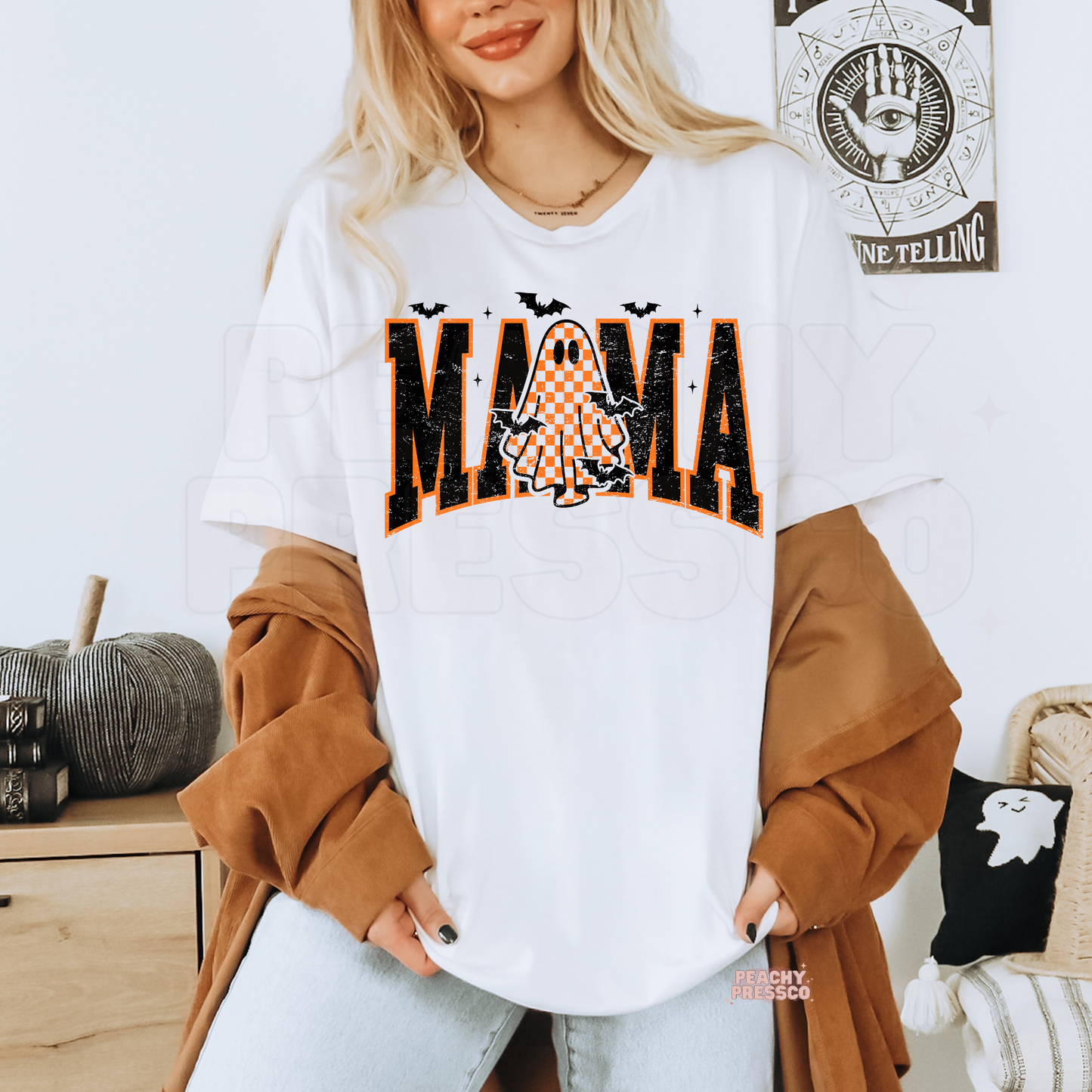 Woman wearing a white t-shirt with a distressed varsity Mama Halloween design featuring an orange checkered ghost, bats and vintage spooky style.