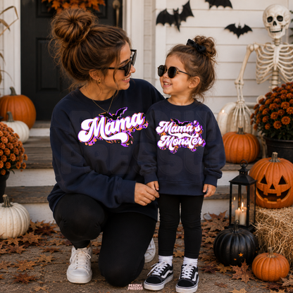 Mom and little girl wearing matching navy Mama and Mama’s Monster Halloween crewneck sweatshirts on a decorated Halloween porch.