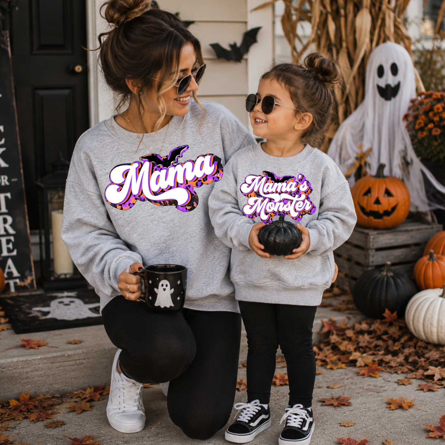 Mama and daughter wearing matching sport grey Mama and Mama’s Monster Halloween sweatshirts with pumpkins and ghost decor.