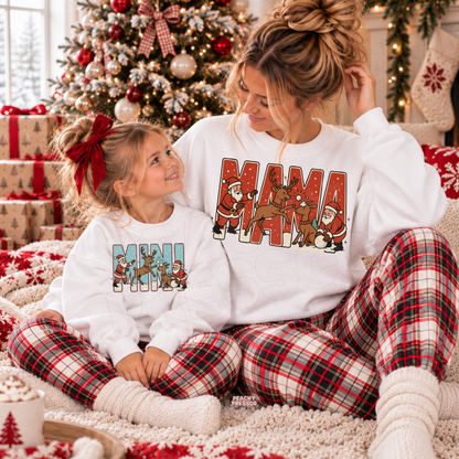 Mom and daughter wearing matching white Mama and Mini Christmas sweatshirts featuring a retro Santa and reindeer design.