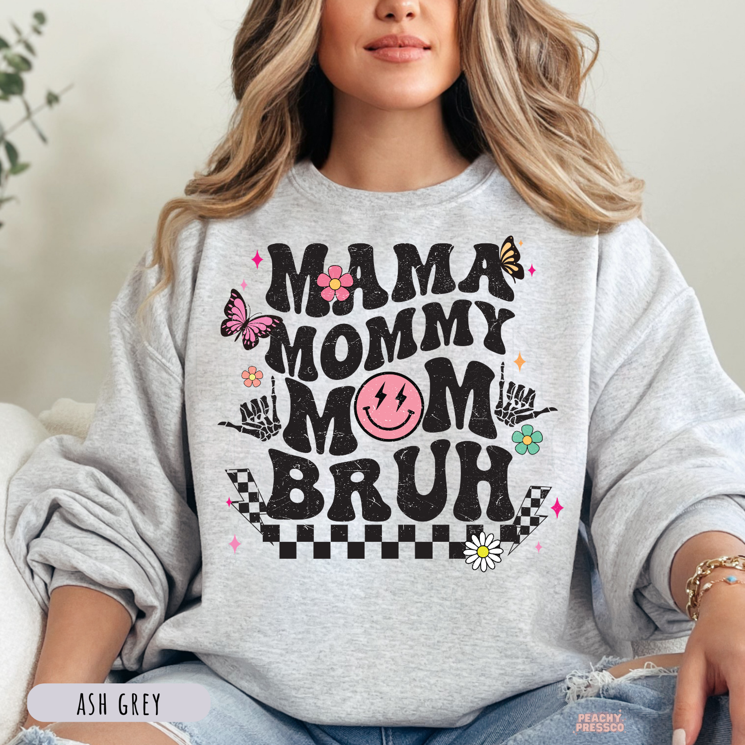 Ash Grey sweatshirt featuring a playful "Mama Mommy Mom Bruh" graphic with vintage-inspired lettering, butterflies, flowers, and checkerboard design.