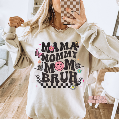 Sand sweatshirt featuring a retro "Mama Mommy Mom Bruh" design with distressed lettering, checkerboard pattern, flowers, and butterflies.