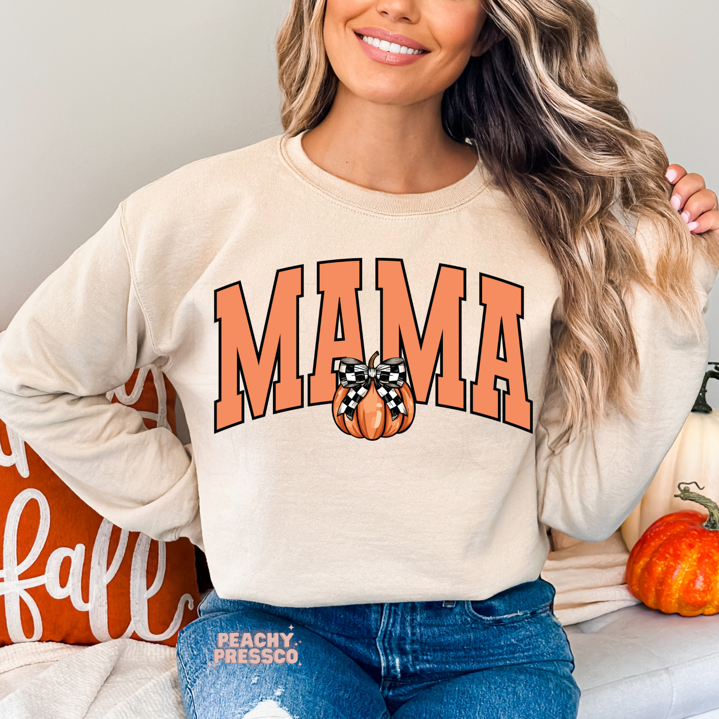 Woman wearing a sand crewneck sweatshirt with a peach Mama graphic and buffalo plaid bow pumpkin design.