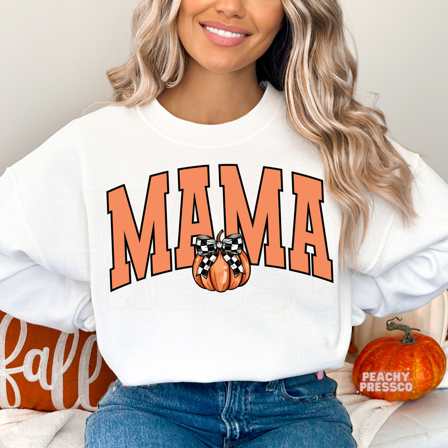 Woman wearing a white crewneck sweatshirt featuring a Mama graphic with a cute pumpkin and buffalo plaid bow.
