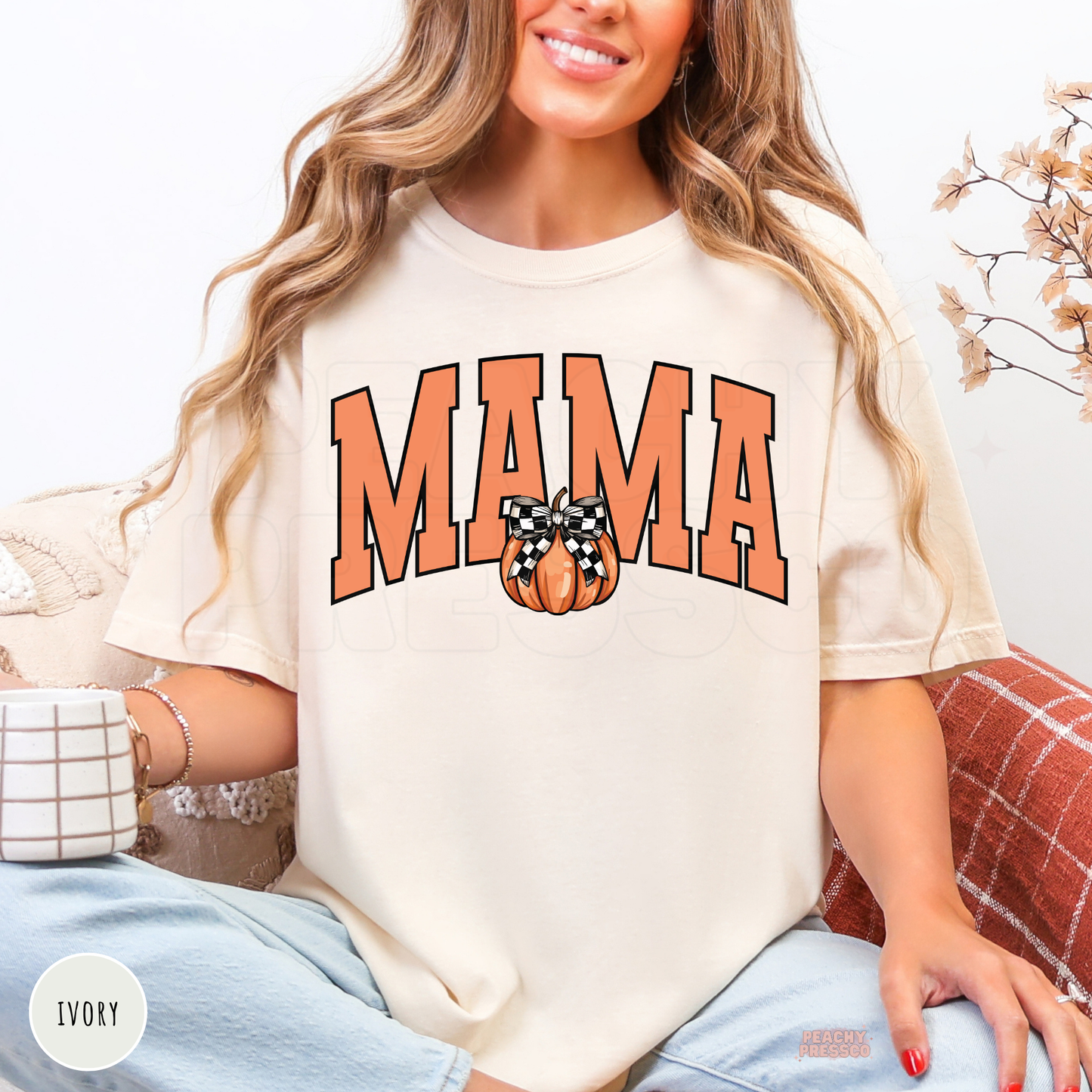 Woman wearing an ivory graphic t-shirt featuring a Mama design with a pumpkin and buffalo plaid bow for autumn.