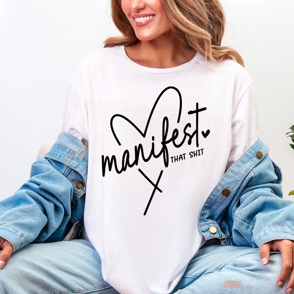 White Manifest That Shit shirt with black script typography, a hand-drawn heart and a funny manifestation quote for positive thinkers.