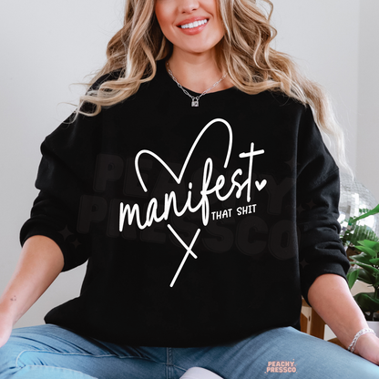 Black Manifest That Shit sweatshirt featuring bold white handwritten lettering, a heart accent and an empowering manifestation quote.