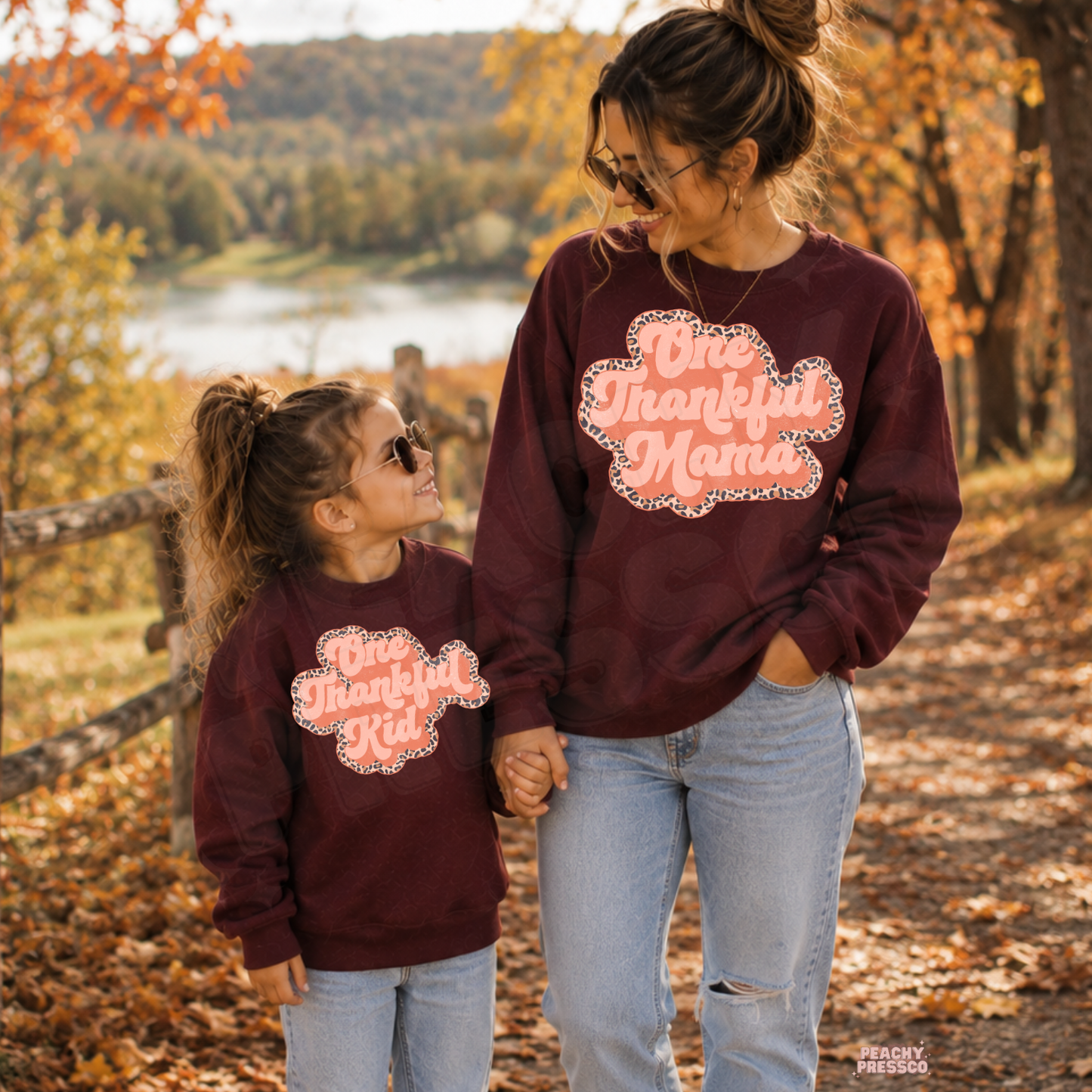 Mama and mini wearing matching maroon One Thankful Mama and One Thankful Kid sweatshirts while walking together in a beautiful fall setting.