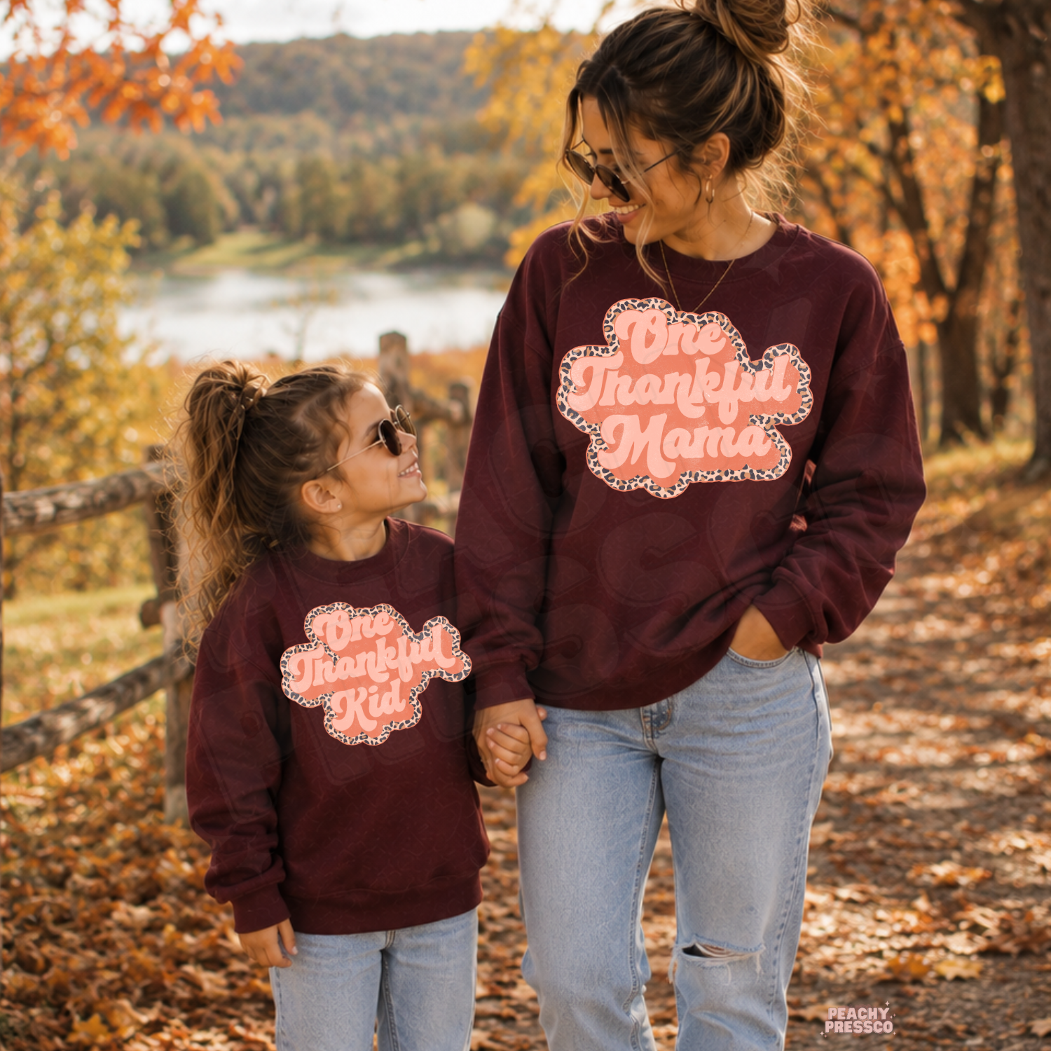 Mama and mini wearing matching maroon One Thankful Mama and One Thankful Kid sweatshirts while walking together in a beautiful fall setting.