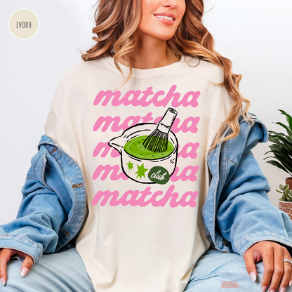 Ivory Matcha Club shirt featuring repeated pink matcha lettering, a bowl of vibrant green matcha tea, bamboo whisk, and cute Matcha Club artwork.