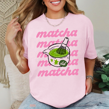 Light pink Matcha Club t-shirt with repeated pink matcha lettering, green matcha tea in a bowl, bamboo whisk, and playful matcha lover design.