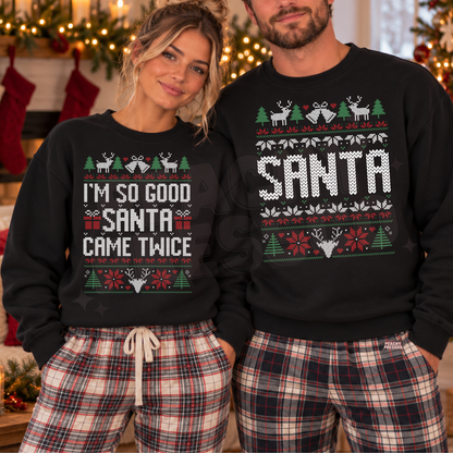 A man and a woman wearing matching black Christmas sweatshirts and plaid pajama pants, standing in a holiday-themed room. The woman's sweatshirt reads 'I'M SO GOOD SANTA CAME TWICE' with festive graphics, and the man's sweatshirt reads 'SANTA' with similar holiday patterns.