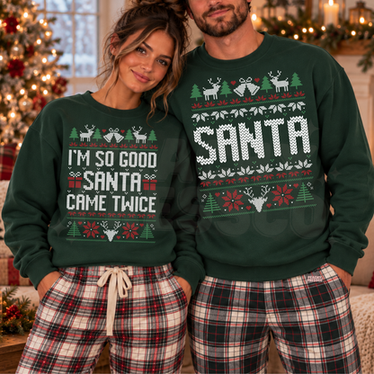 A couple wearing matching forest green Christmas sweaters with festive holiday graphics and text, paired with red and black plaid pajama pants, posed in front of a decorated Christmas tree and warm holiday lights.