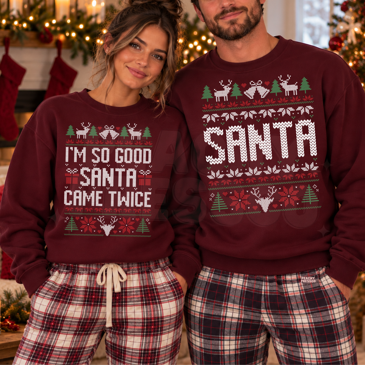 A man and a woman wearing matching burgundy Christmas sweaters with holiday graphics and text, paired with plaid pajama pants in a festive indoor setting with Christmas lights and stockings in the background.