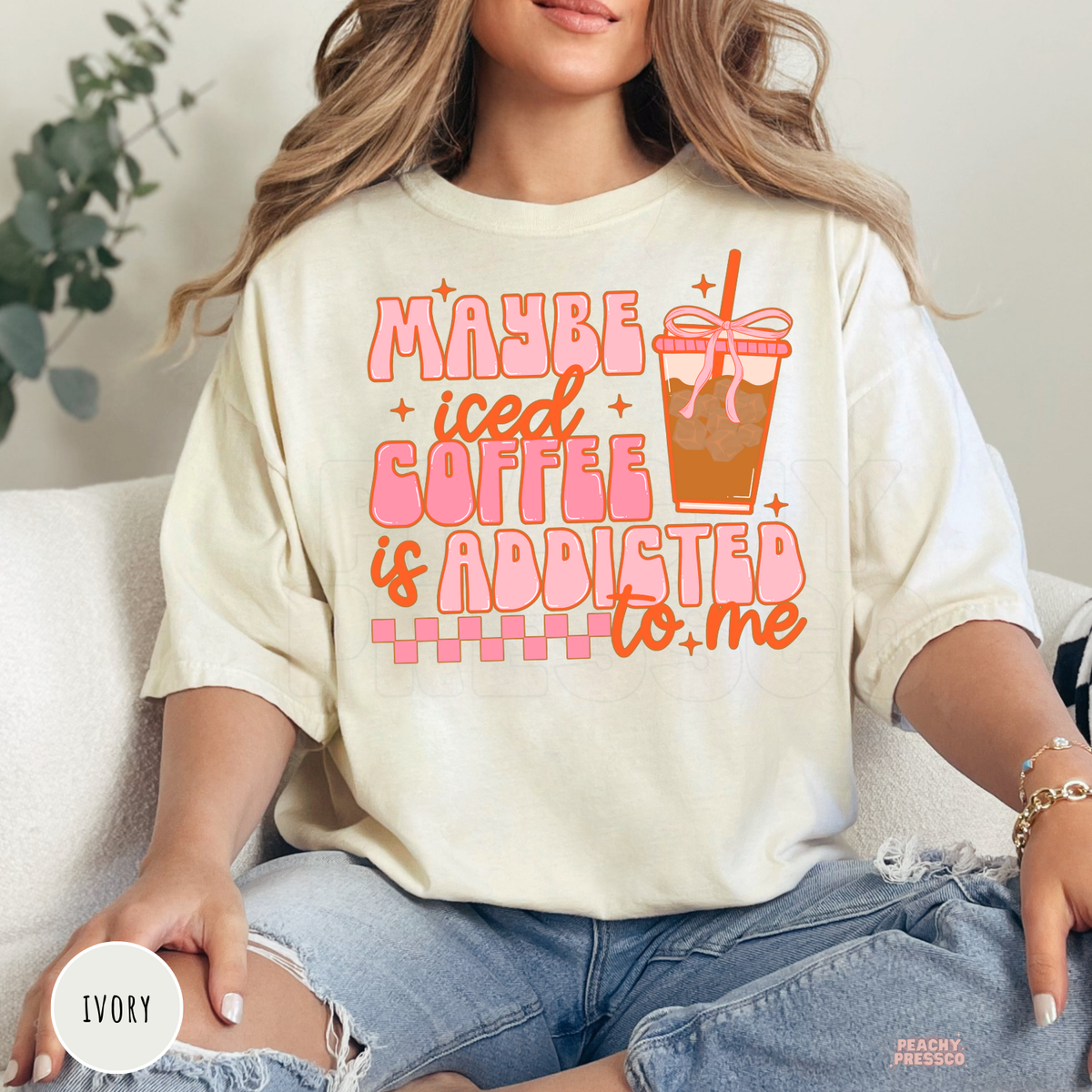 Ivory graphic t-shirt featuring the "Maybe Iced Coffee Is Addicted to Me" quote in retro lettering with a pink iced coffee cup design.