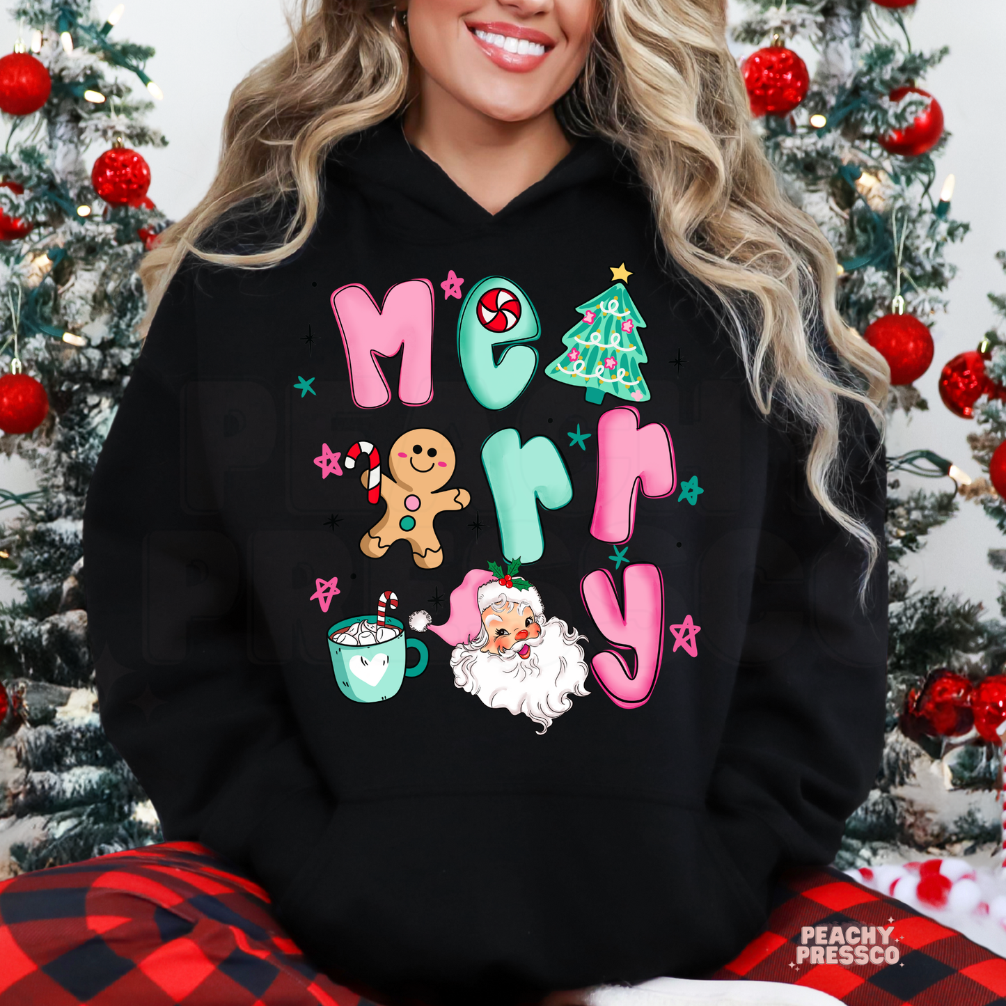 Woman wearing a black Christmas hoodie with a colorful Merry Christmas graphic featuring Santa, gingerbread man, Christmas tree and candy cane.
