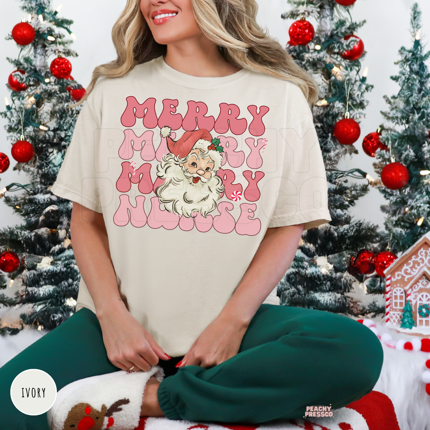 A woman wearing a ivory colored t-shirt with a pink and white 'Merry Merry Nurse' graphic featuring a cartoon Santa Claus, sitting in front of decorated Christmas trees.