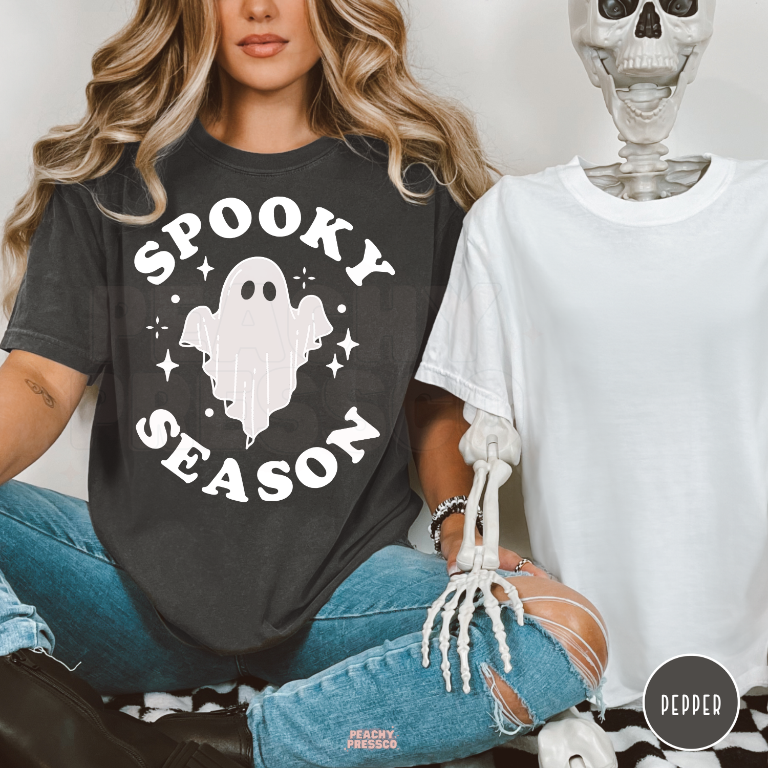 Woman wearing a pepper Comfort Colors t-shirt featuring a minimalist Spooky Season ghost graphic with a Halloween skeleton prop.