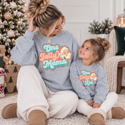 Mom and daughter wearing matching sport grey One Jolly Mama and One Jolly Kid Christmas crewneck sweatshirts.