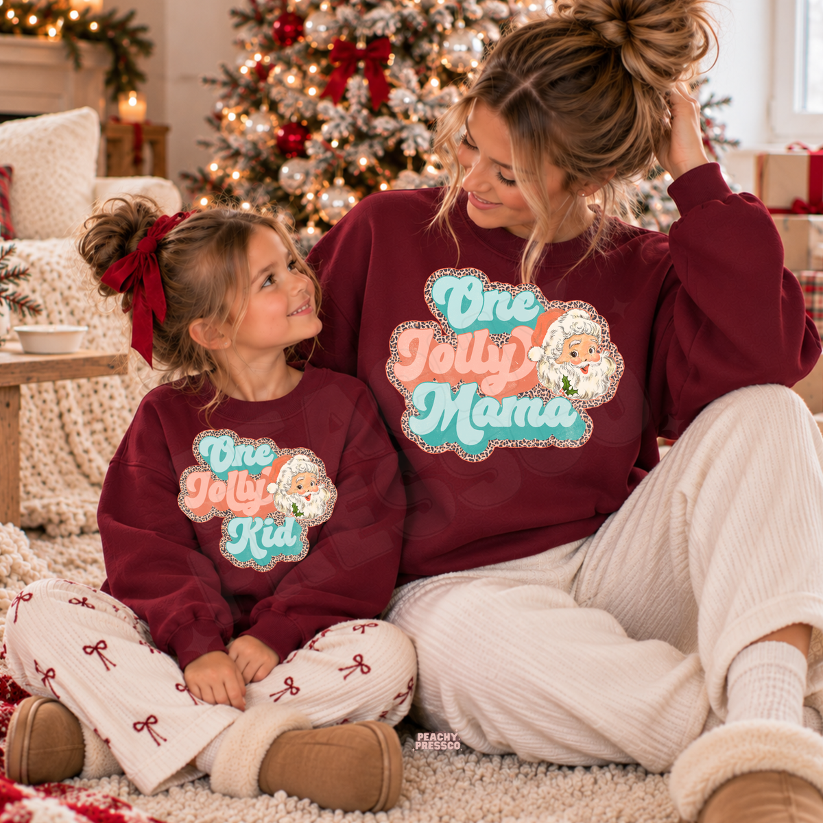Mom and daughter wearing matching maroon One Jolly Mama and One Jolly Kid Christmas sweatshirts with vintage Santa design.