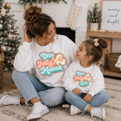 Mom and daughter wearing matching white One Jolly Mama and One Jolly Kid Christmas sweatshirts with retro Santa graphic.