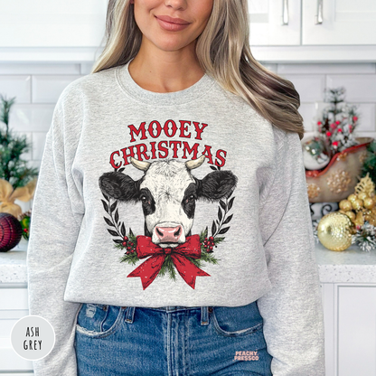 Women wearing an ash grey Mooey Christmas cow wreath crewneck sweatshirt in a kitchen setting.