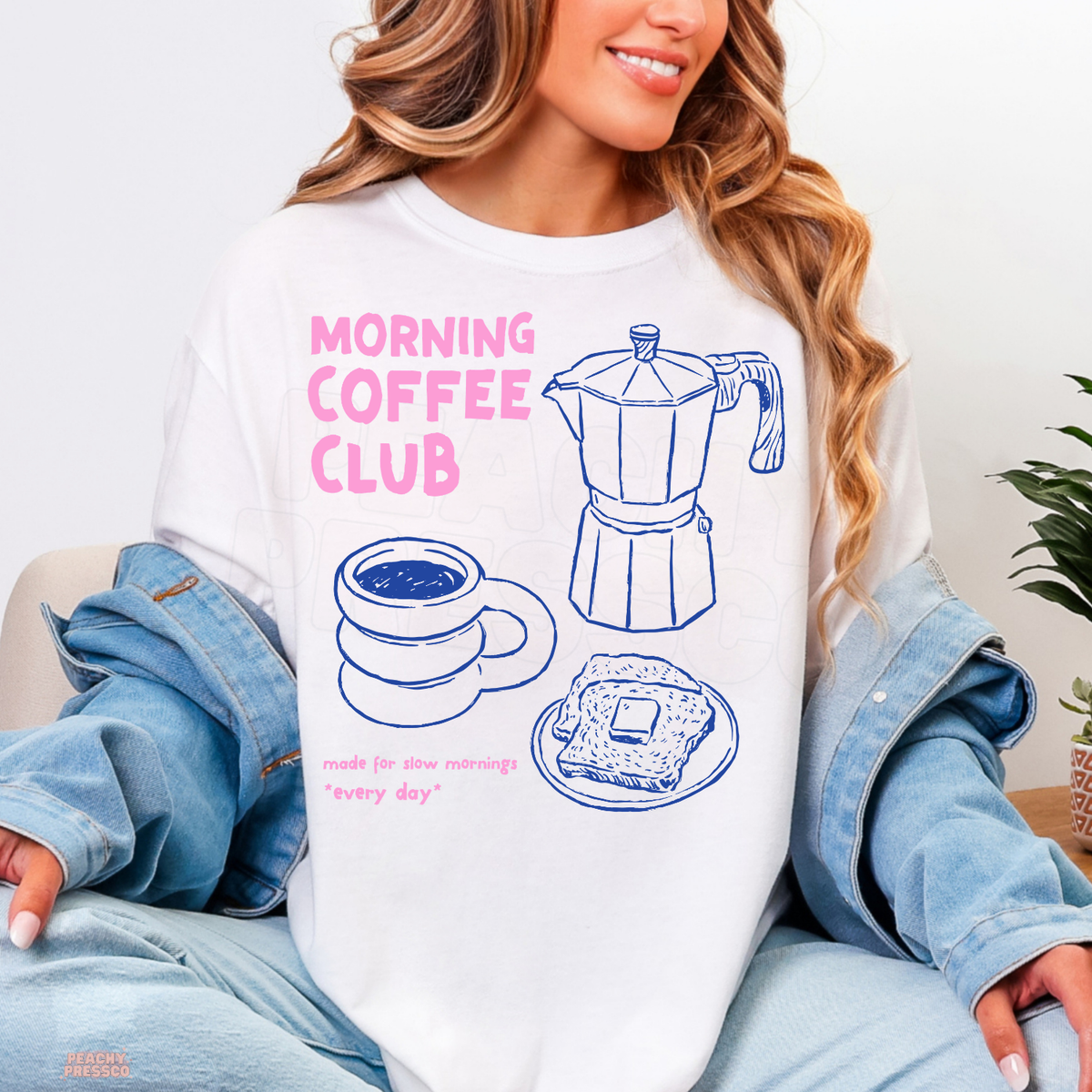 White Morning Coffee Club shirt featuring a blue illustrated espresso maker, coffee mug, toast and playful pink lettering celebrating slow mornings.