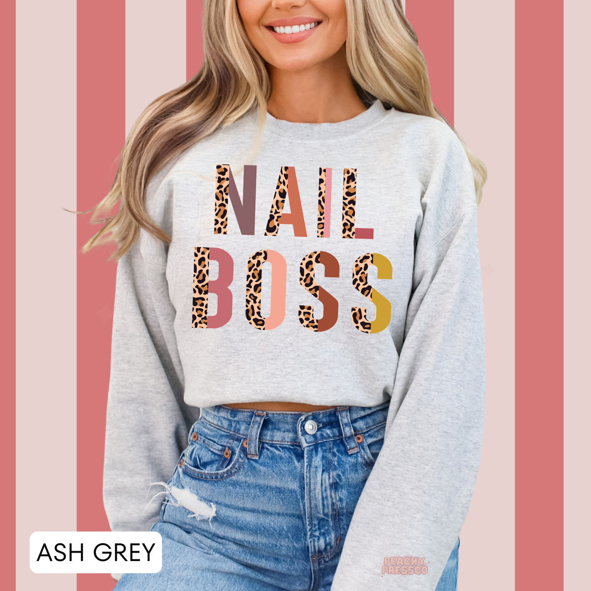Woman wearing an ash grey Nail Boss crewneck sweatshirt featuring colorful leopard print lettering, a fun design for nail technicians.