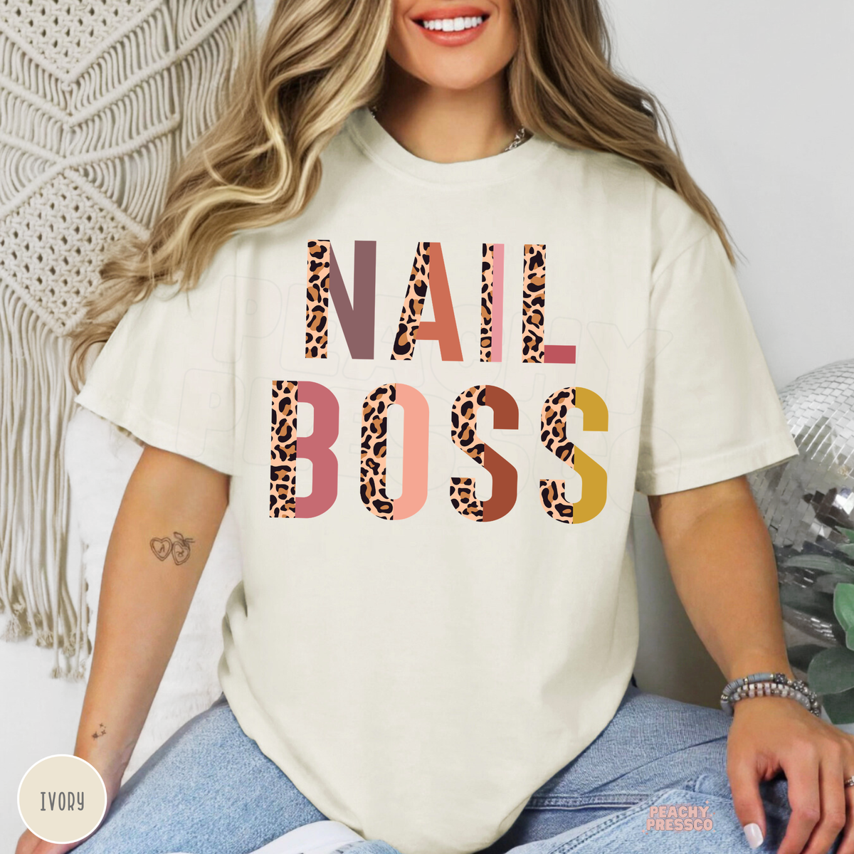 Woman wearing an ivory Nail Boss graphic T-shirt with trendy leopard print lettering, designed for nail technicians and manicurists.