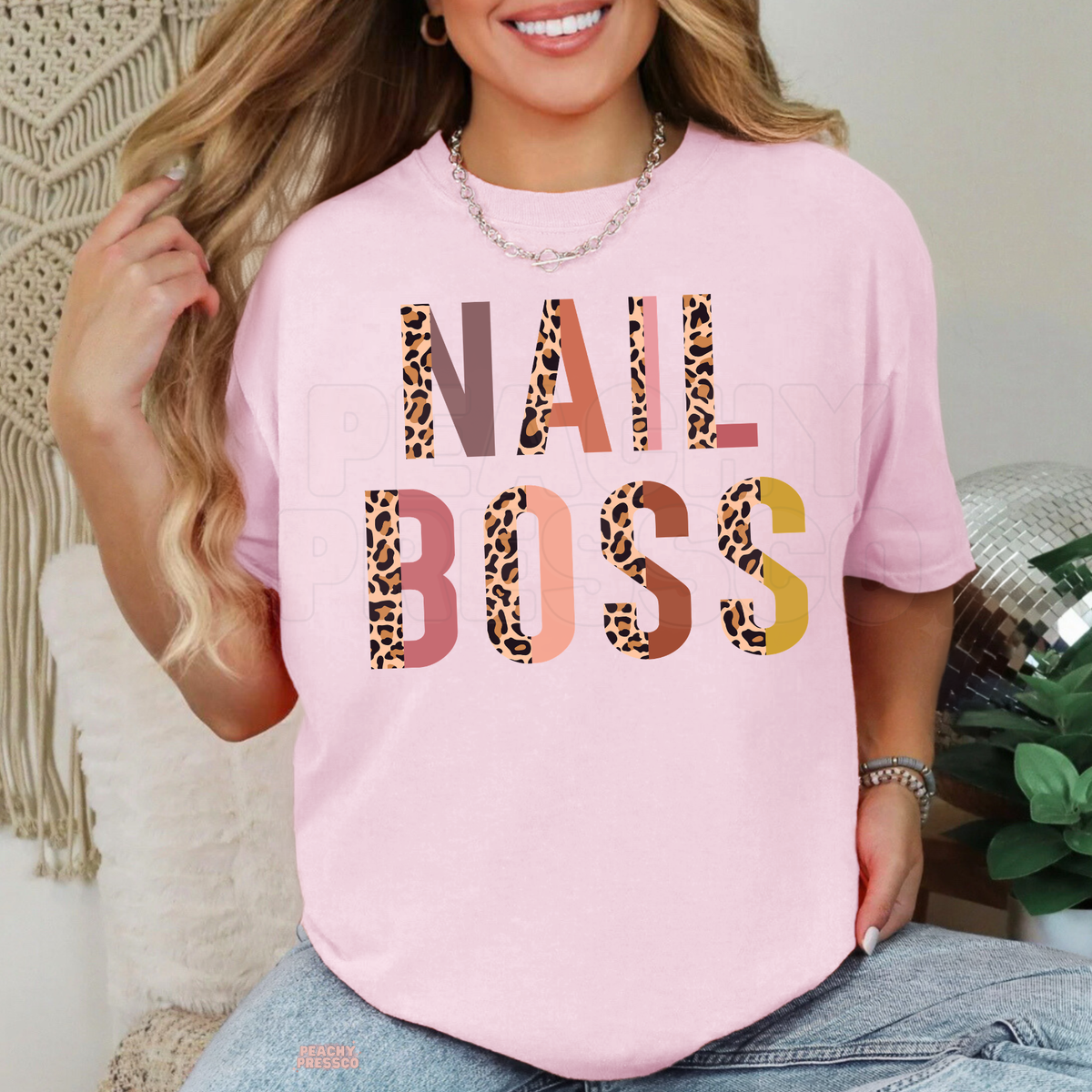 Woman wearing a light pink Nail Boss graphic T-shirt with colorful leopard print typography, a cute gift idea for nail techs.