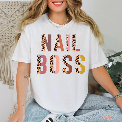 Woman modeling a white Nail Boss T-shirt featuring bold leopard print letters in pink, coral, brown and mustard tones.