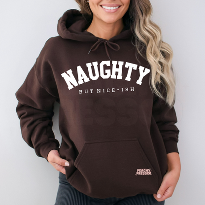 A woman wearing a dark brown pullover hoodie with 'NAUGHTY BUT NICE-ISH' printed in white on the front. The hoodie has a drawstring hood and a pocket.
