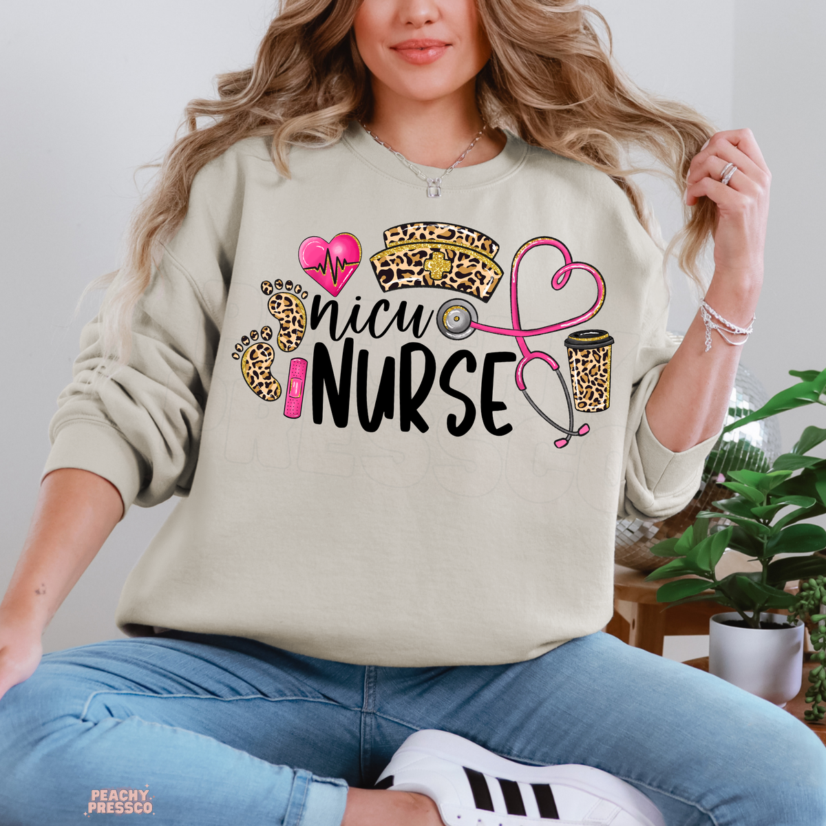 Sand NICU nurse crewneck sweatshirt with black NICU Nurse lettering, leopard print nursing hat, baby footprints and pink medical heart graphics.