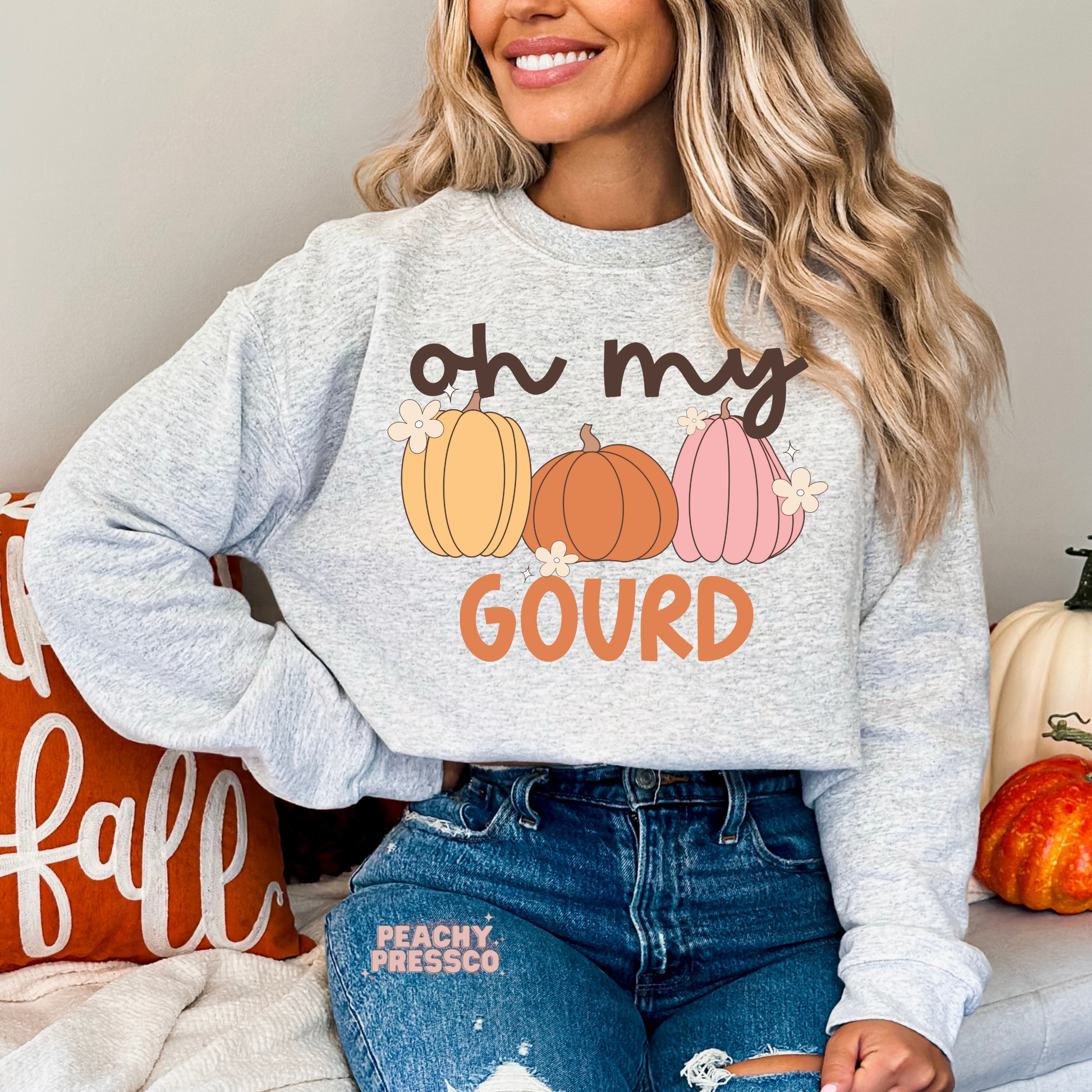 Woman wearing an ash grey crewneck sweatshirt with a cute "Oh My Gourd" pumpkin graphic in soft fall colors.
