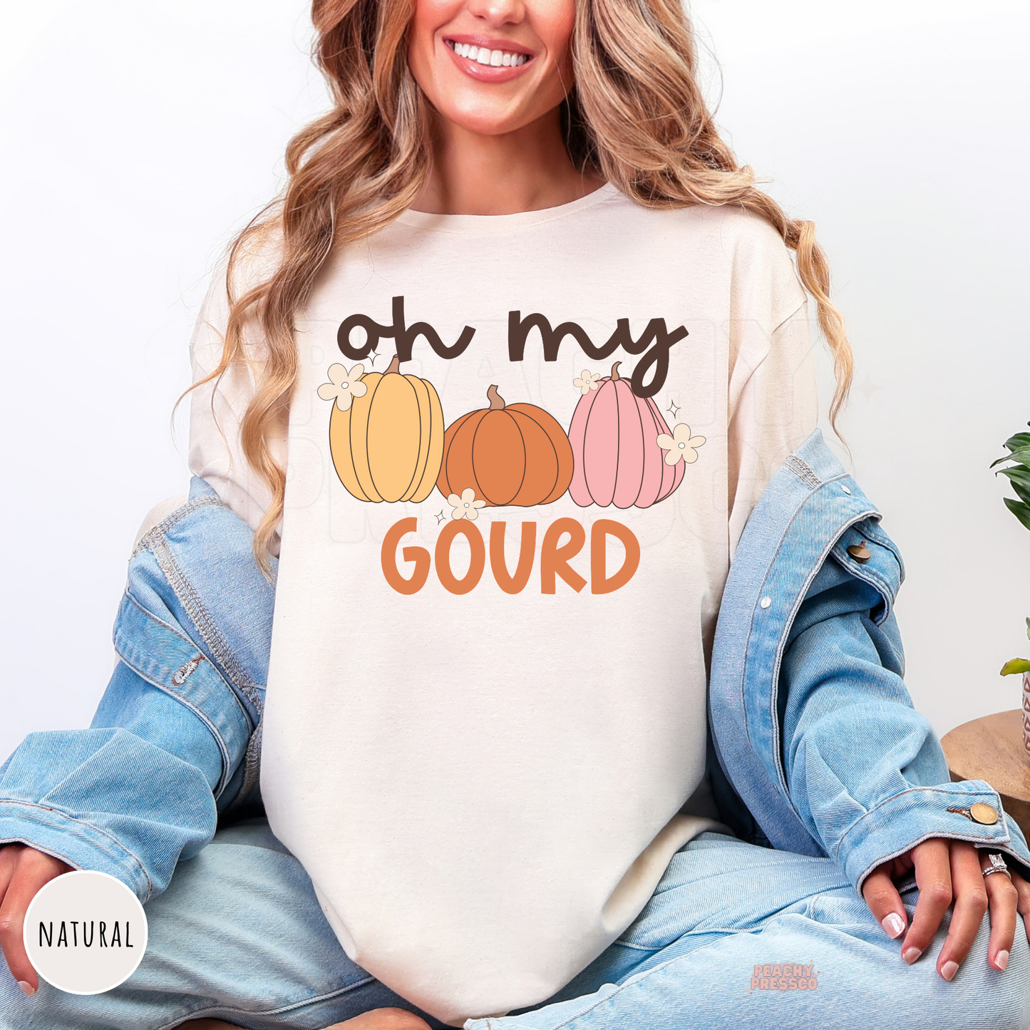Woman wearing a natural t-shirt featuring a trendy "Oh My Gourd" pumpkin graphic with pink, orange, and yellow pumpkins.