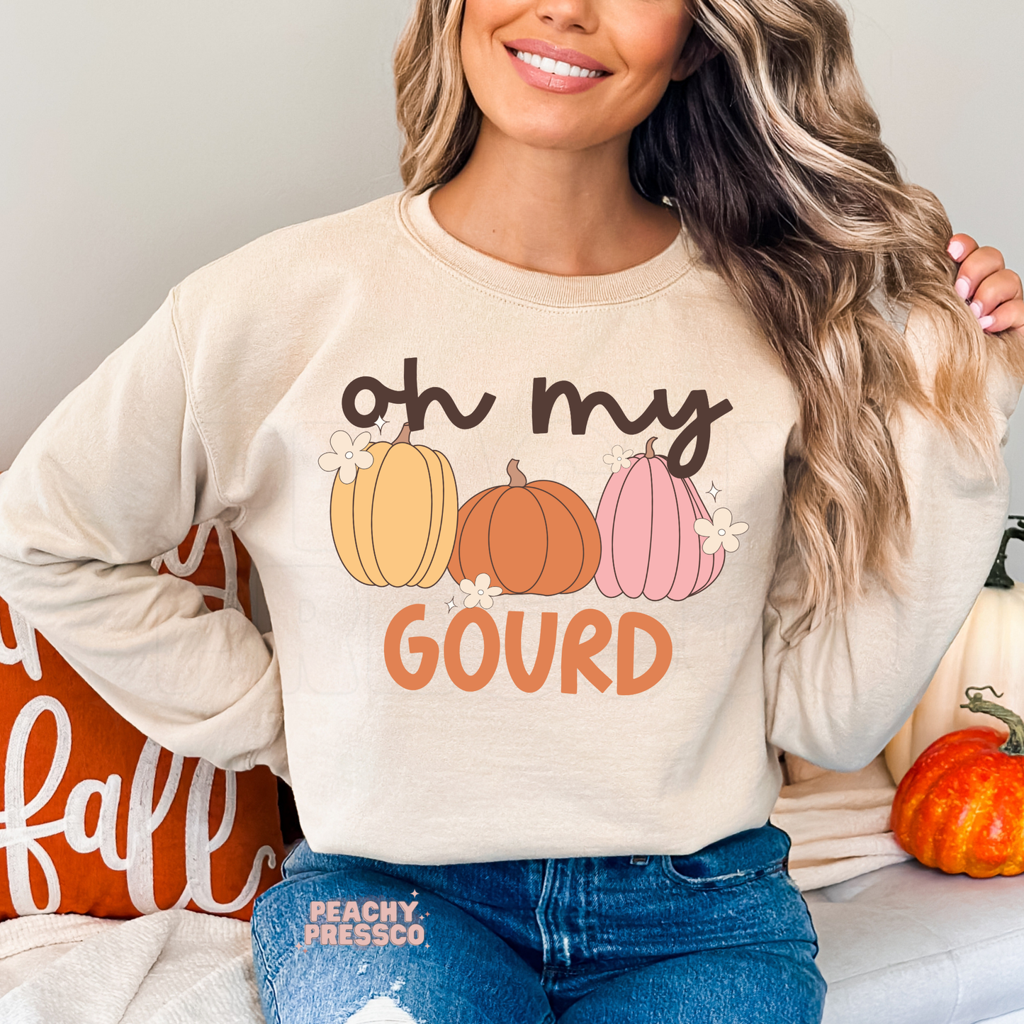 Woman wearing a sand crewneck sweatshirt featuring an "Oh My Gourd" graphic with pastel pumpkins in yellow, orange, and pink for fall.