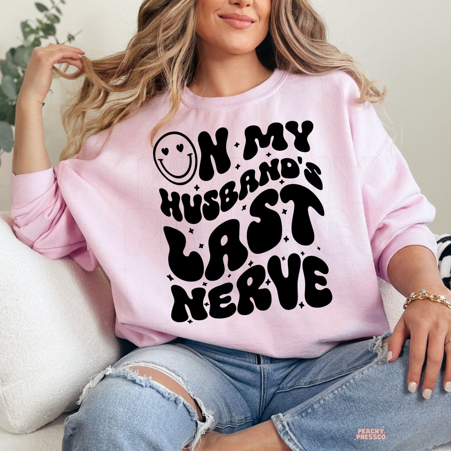 Light pink sweatshirt featuring a humorous "On My Husband's Last Nerve" graphic with oversized retro lettering. Cute wife gift for anniversaries or birthdays.