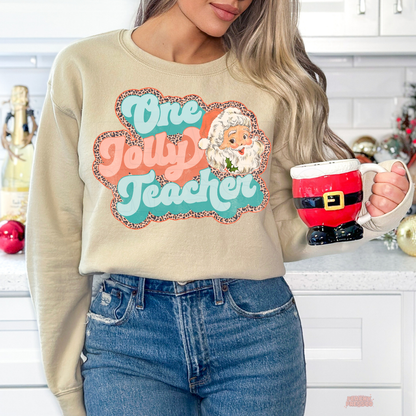 Woman in a kitchen holding a red Santa boot mug, wearing a sand crewneck sweatshirt printed with the retro One Jolly Teacher design.