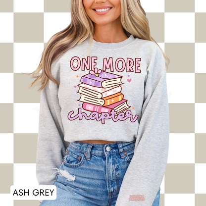 Ash Grey crewneck sweatshirt featuring a colorful stack of books with the phrase "One More Chapter," perfect for book lovers and readers.