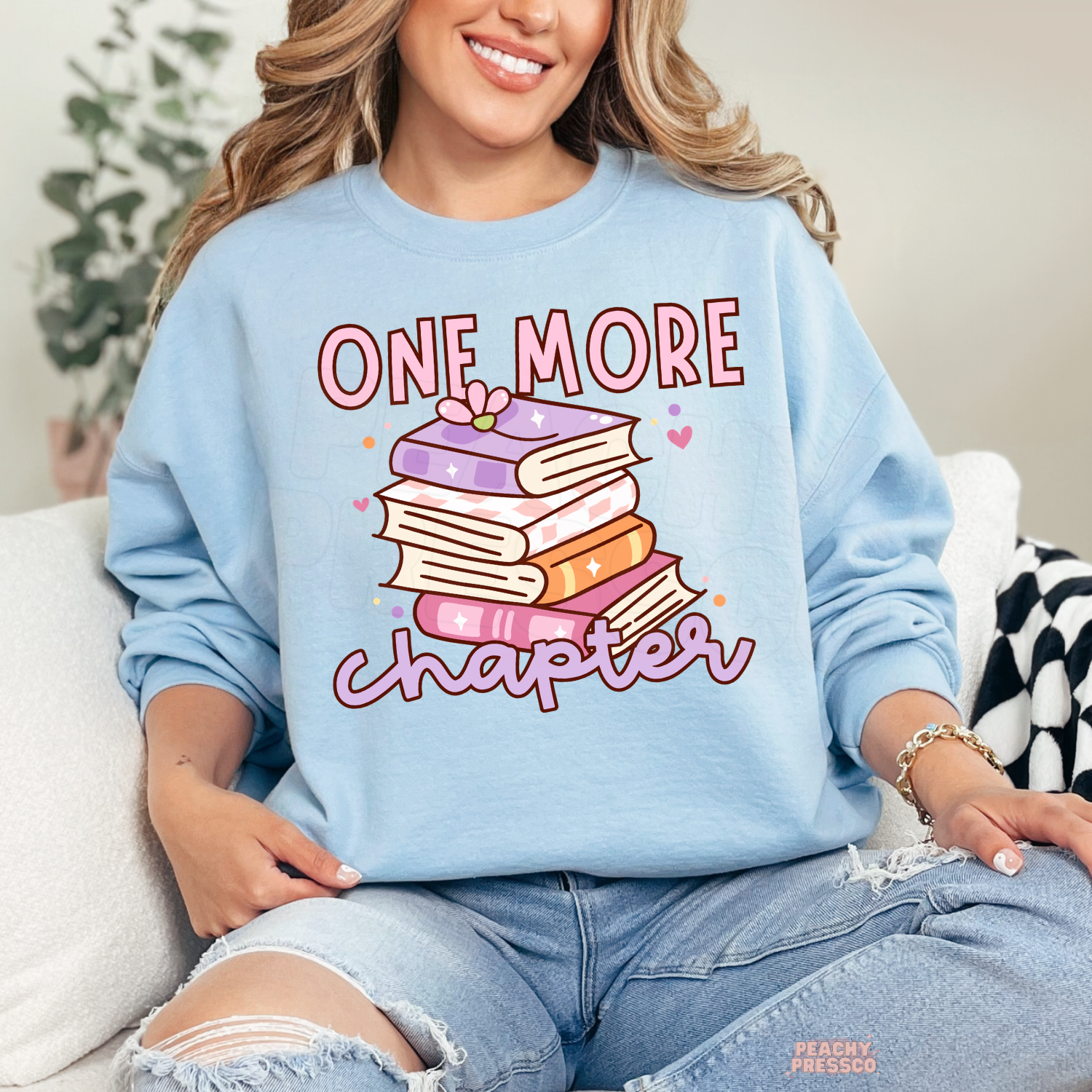 Light blue crewneck sweatshirt with a pastel stack of books and "One More Chapter" graphic, perfect for cozy reading outfits.