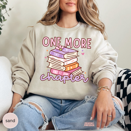Sand crewneck sweatshirt featuring a pastel book stack and "One More Chapter" graphic for readers and cozy book lovers.