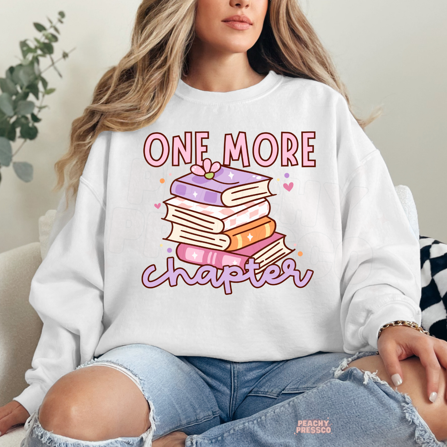 White crewneck sweatshirt with a pastel stack of books and "One More Chapter" graphic, ideal for cozy reading days and bookworms.